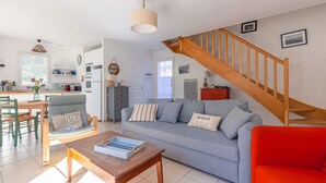 Una sala de estar con un sofá, una silla roja, una mesa de madera, una escalera y una cocina al fondo.