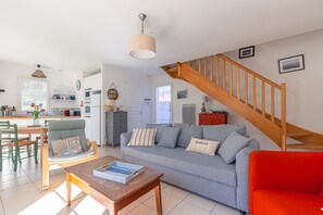 Ein Wohnzimmer mit einer Couch, einem roten Sessel, einem Holztisch, einer Treppe und einer Küche im Hintergrund.