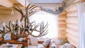 L’intérieur d’un chalet confortable, avec des murs en rondins, un canapé en cuir, un lustre et un filet suspendu.