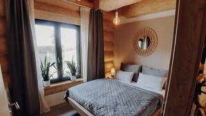 Une chambre confortable avec un grand lit, une fenêtre avec des rideaux, une plante en pot et un miroir rond accroché au mur.