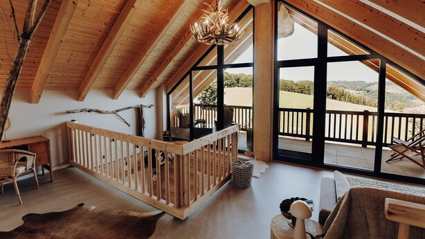 Une pièce spacieuse avec un plafond haut, des poutres en bois, une grande fenêtre et une vue sur l’extérieur.