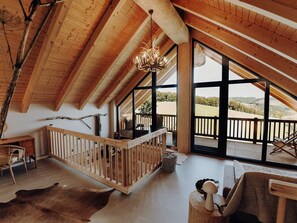 Ruime kamer met een hoge plafond, houten balken, een groot raam en uitzicht op de omgeving.