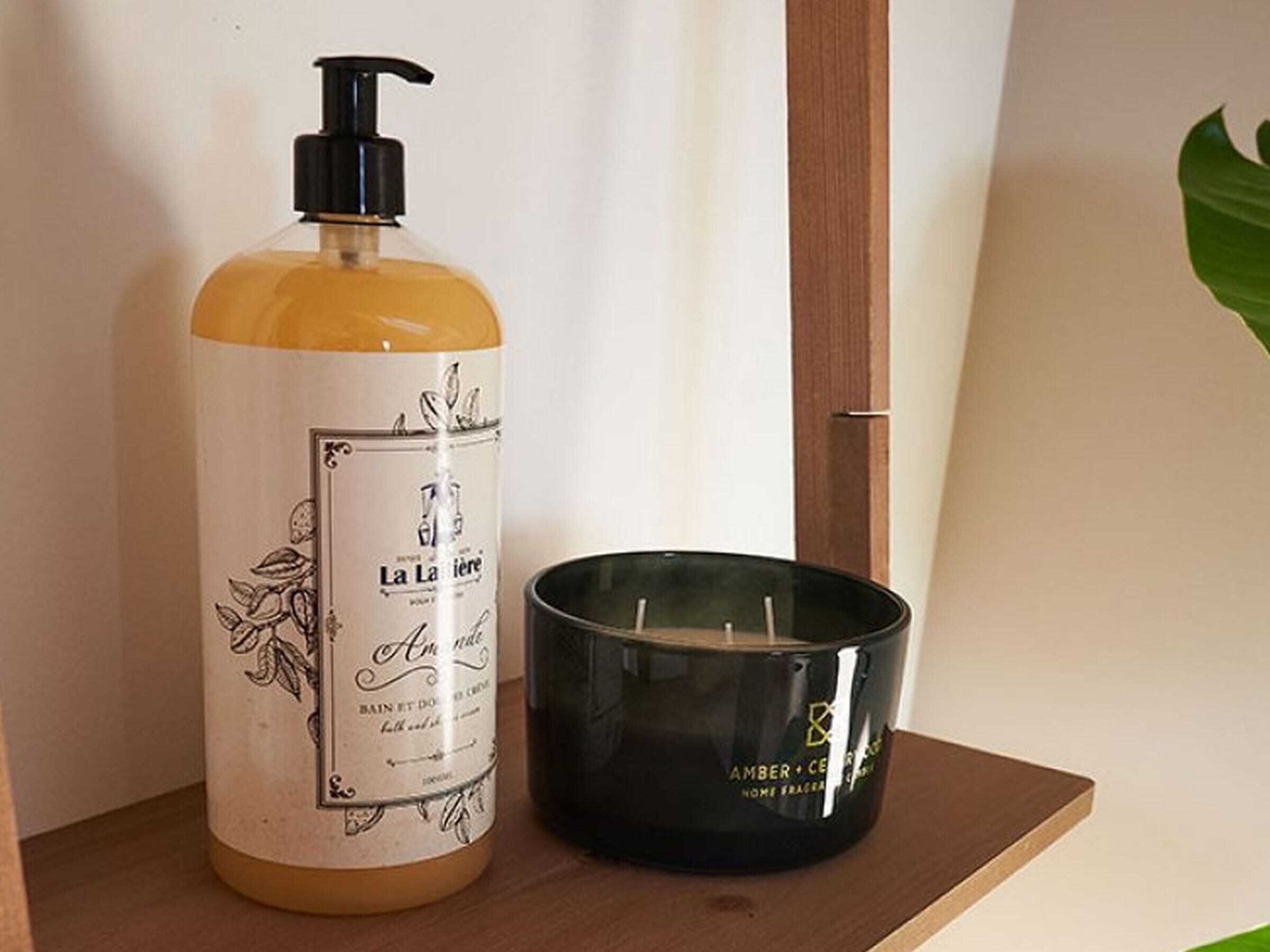 Une bouteille de gel douche La Laitière et une bougie noire sur une étagère en bois.