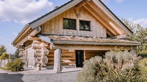 Une cabane en rondins avec un toit en pente, une véranda et un petit jardin.