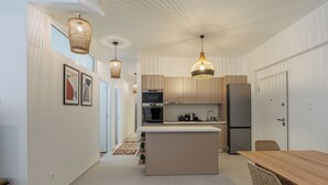 A modern kitchen with a central island, pendant lighting, and a dining area with a wooden table and chairs. - Cozy and Spacious Apartment close to the Acropolis (Athina)