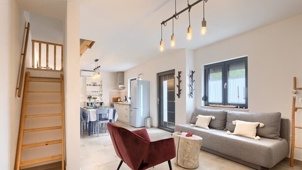 A modern living room with a sofa, a red chair, and a wooden ladder. - House Lando (74318-K1) - Pula (Pula)