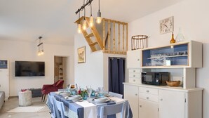 A dining area with a table set for four, a kitchen with a microwave and cabinets, and a staircase with exposed beams. - House Lando (74318-K1) - Pula (Pula)