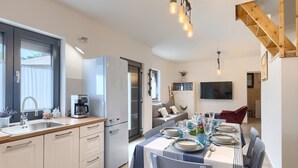 A modern kitchen with a built-in oven, a coffee machine, and a sink. There is a dining area with a table set for four, and a staircase leading to an upper level. - House Lando (74318-K1) - Pula (Pula)