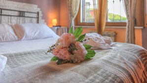 Una cama con un arreglo floral, una ventana con cortinas y una lámpara de noche.