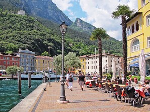 A waterfront promenade with outdoor seating, a historic building, and a mountain backdrop. - Villa im Grünen in Riva del Garda mit Terrasse by Interhome (Riva del Garda)