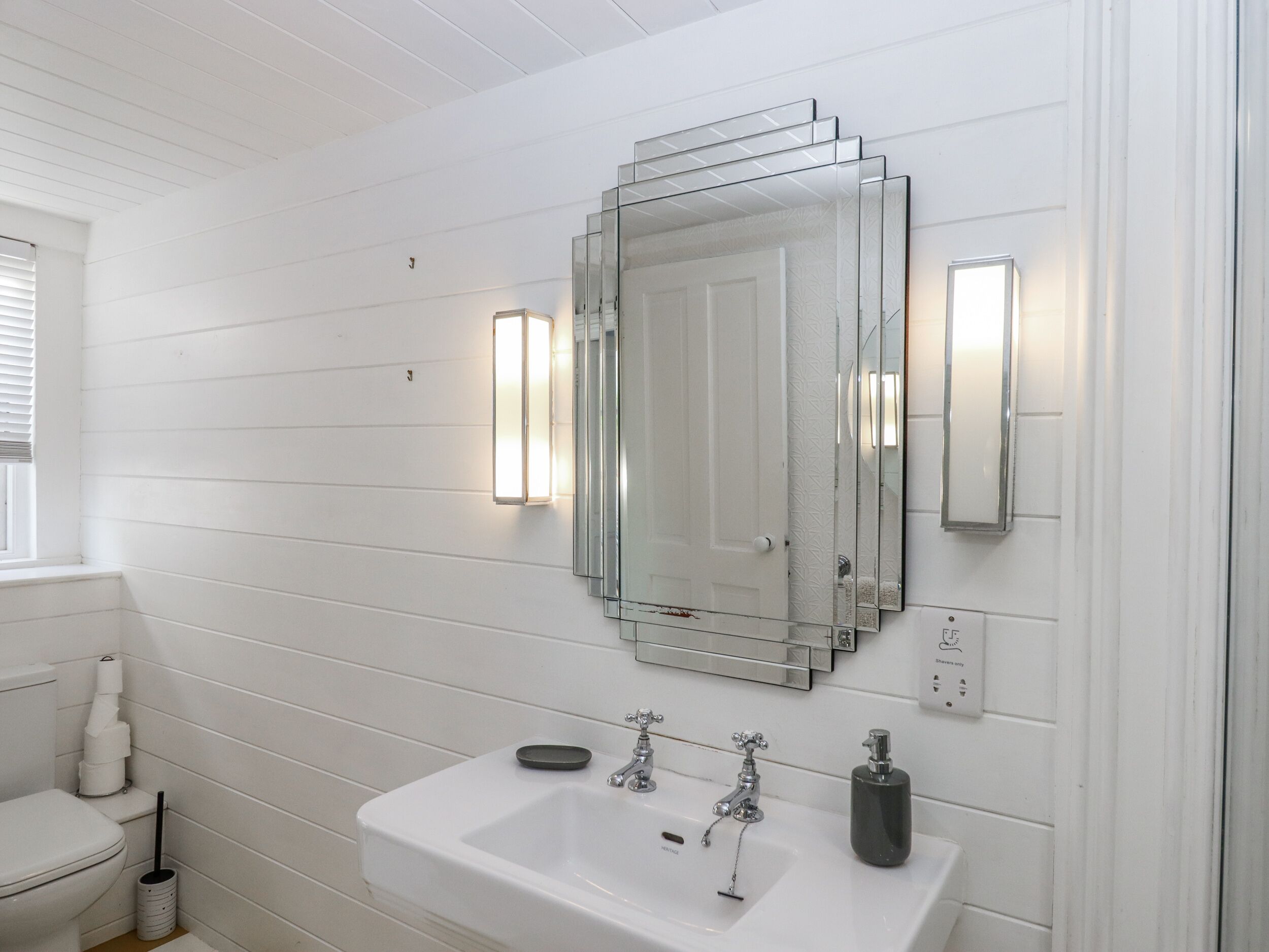 A bathroom with a white sink, two faucets, a soap dispenser, and a mirror with a decorative frame.