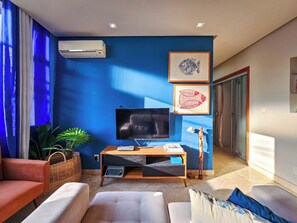 A modern living room with a flat-screen TV, comfortable seating, and artwork on the walls. - Apto com 3 Quartos Ar e Wi-fi a 100m da Praia (Salvador)