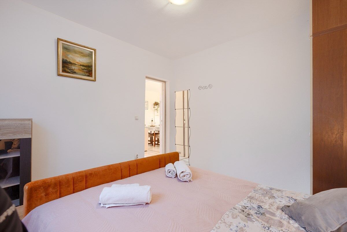 A bedroom with a bed, a nightstand, a mirror, and a painting on the wall.
