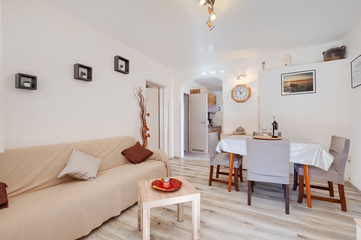 Een moderne woonkamer met een beige bank, een klein houten tafeltje en een eethoek met een witte tafelkleed en stoelen.