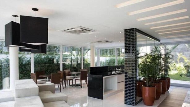 Una cocina moderna con encimera negra, armarios blancos y un amplio ventanal con vistas a un jardín. Hay una zona de comedor con un sofá blanco y una mesa de centro.