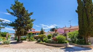 A courtyard with stone paving, surrounded by houses with red-tiled roofs, and lush greenery including trees and flowering plants. - Apartments and Room Vjera (76011-A1) - Medulin (Medulin)