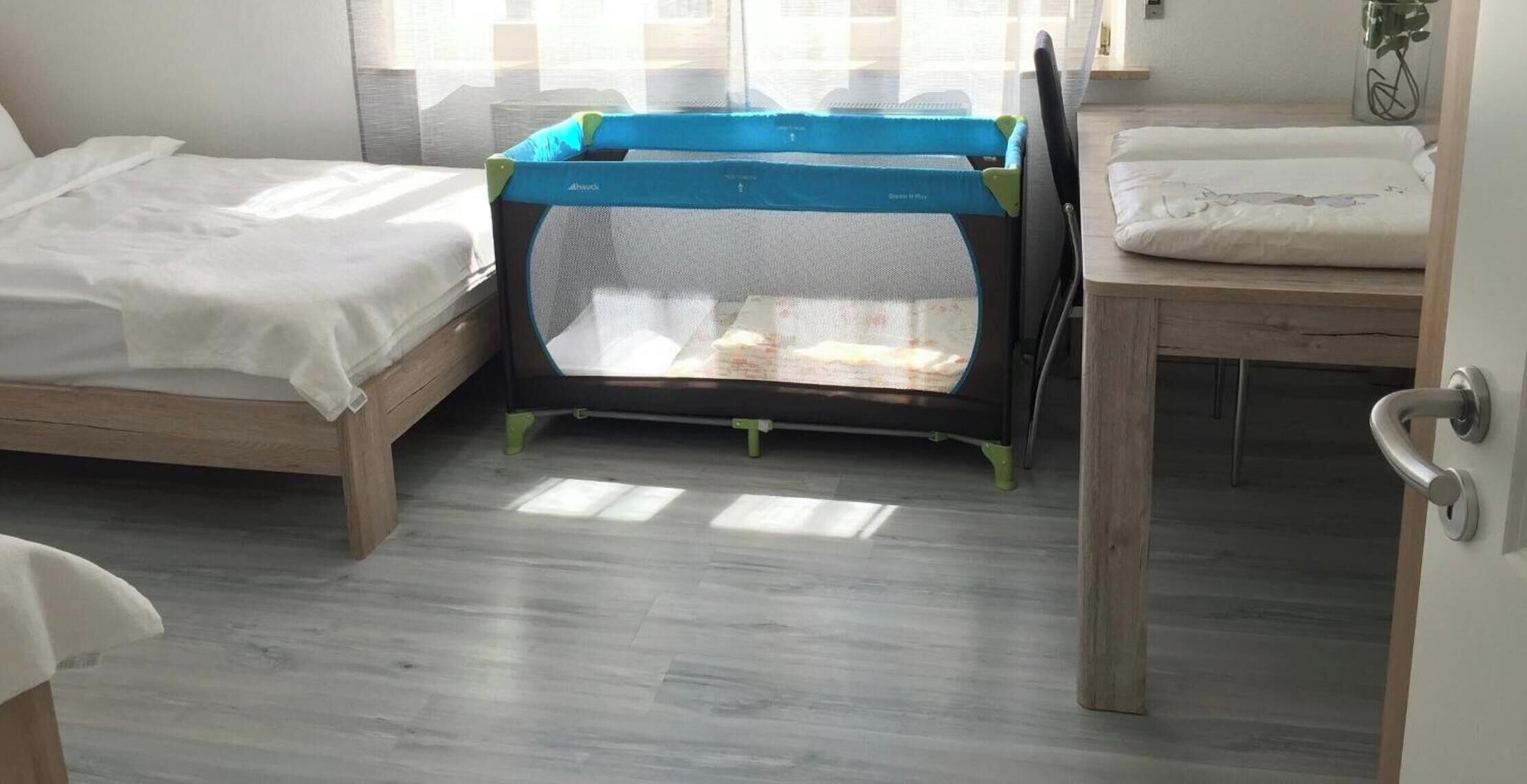 Une pièce avec un lit, une petite table et un parc pour bébé.