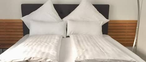 A double bed with white linens, a wooden headboard, and a white furry throw on the footboard.