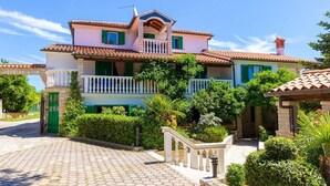 Ein zweigeschossiges Haus mit Balkon, steinernen Eingang und gepflasterter Auffahrt.