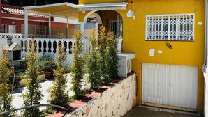 A yellow building with a tiled roof, a white door, and a small garden area with potted plants. - Family-friendly house with Garden, 4 Minutes from the Beach (Cambrils)