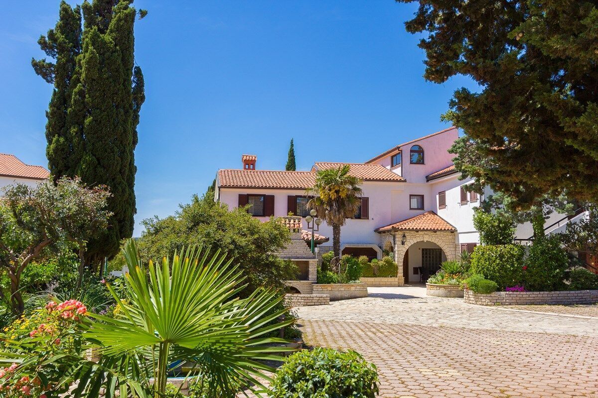 A traditional Mediterranean-style villa with a courtyard, stone pathway, and lush greenery.