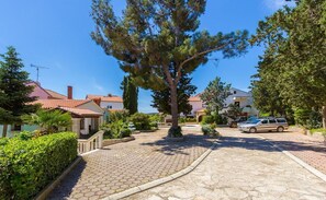 A residential area with paved pathways, a large tree, and houses with red-tiled roofs. - Apartments and Room Vjera (76011-A5) - Medulin (Medulin)