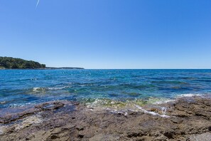 Uma costa rochosa com águas azuis cristalinas e um continente ao longe.