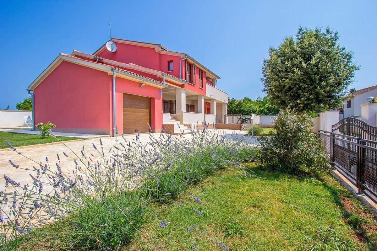 A two-story house with a red facade, a front entrance, and a small garden with lavender plants.