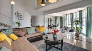 Een ruime woonkamer met een hoekbank, een ronde salontafel en een eethoek op de achtergrond.