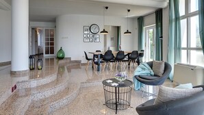 Een ruime woonkamer met een eettafel, stoelen, een ronde salontafel en een comfortabele zithoek met een bank en fauteuil.