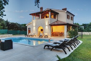 Ein zweistöckiges Haus mit Swimmingpool, Sitzgelegenheit im Freien und einer Steinaußenwand.