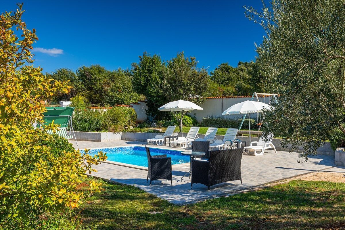 A swimming pool with lounge chairs and umbrellas, surrounded by greenery.