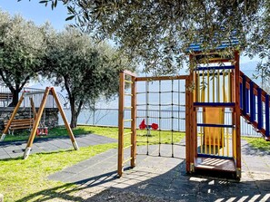 Ein Spielplatz mit Schaukeln, einer Kletterkonstruktion und einem eingezäunten Bereich mit Blick auf das Wasser.