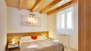 Una camera da letto con soffitto in legno, un letto con copriletto color beige, un cuscino rosso e un quadro con dei velieri appeso al muro.