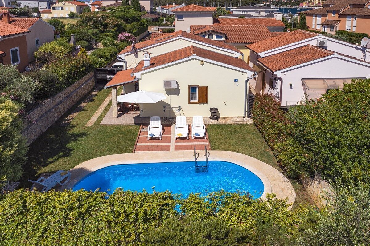 A residential property with a swimming pool, white lounge chairs, and a covered patio area.
