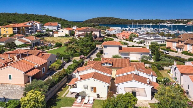 Una zona residenziale costiera con case, una piscina e un porto turistico sullo sfondo.