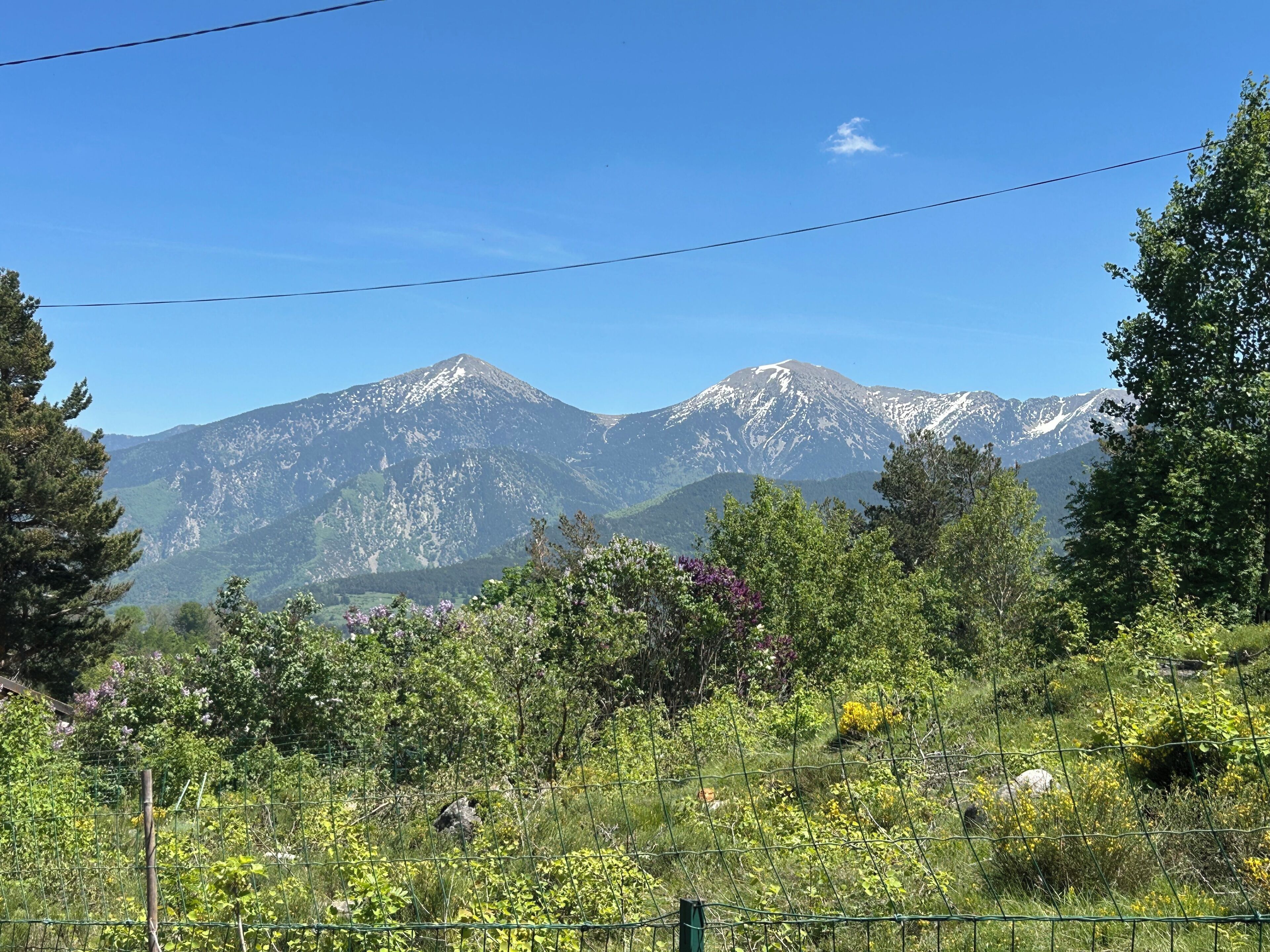 A mountainous landscape with a clear sky, a fence in the foreground, and a variety of vegetation.