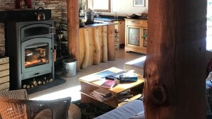 A rustic cabin interior with a stone wall, wooden beams, a fireplace, wicker furniture, and a kitchen area. - A B&B in the heart of Chalet Mitja, calm and well-being guaranteed! (La Cabanasse)