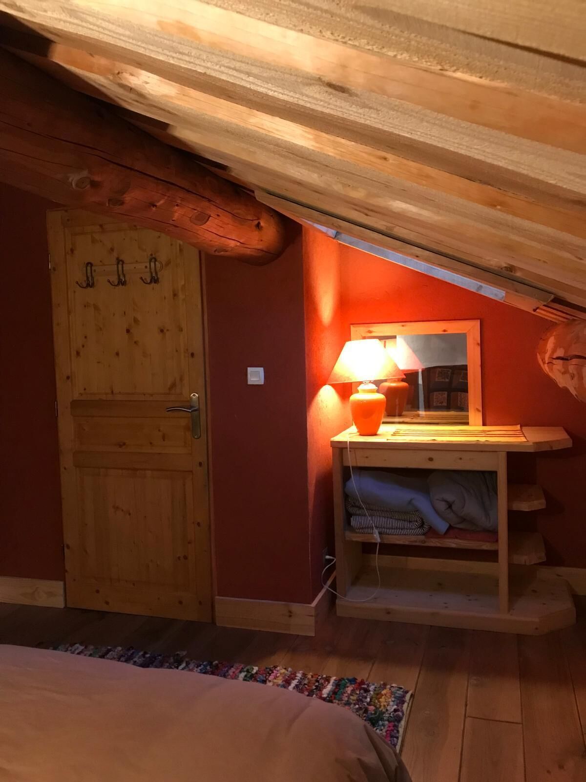 Et soveværelse med en trædør, et sengebord med en lampe, et spejl og en seng.