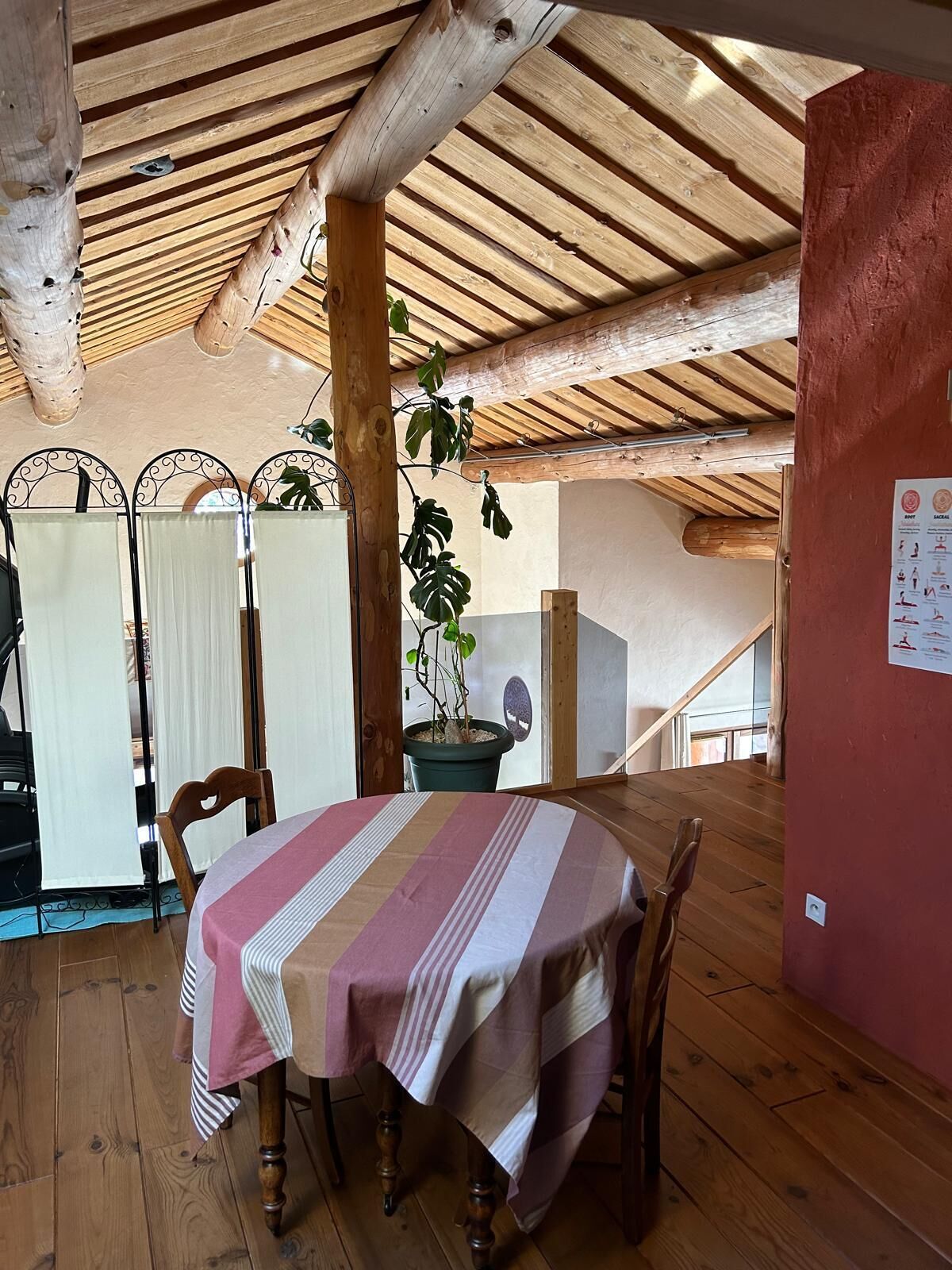 A wooden dining area with a table covered by a striped tablecloth, wooden chairs, and a potted plant.