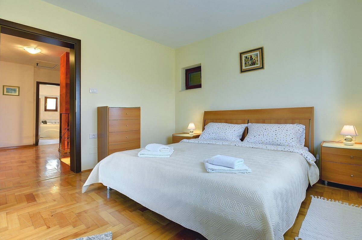 Une chambre à coucher avec un lit en bois, deux tables de chevet avec des lampes, une petite fenêtre et une porte donnant sur une autre pièce.
