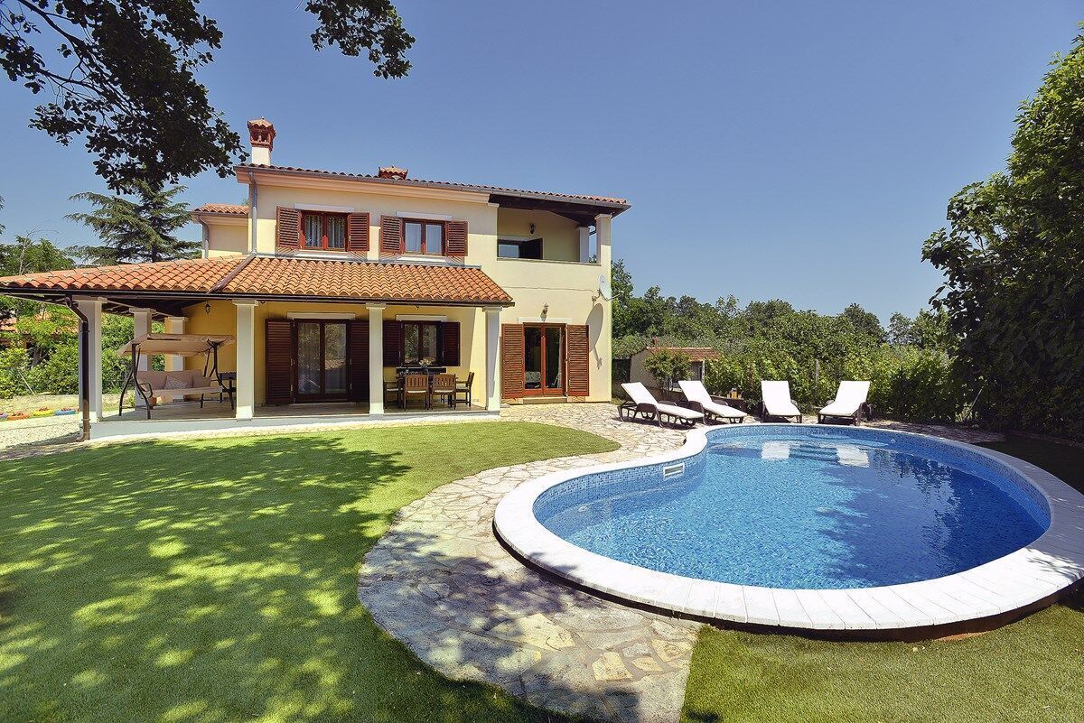 A two-story house with a swimming pool, a patio with chairs, and a lawn.