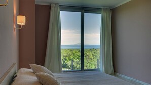 Un dormitorio con un ventanal grande, una cama con ropa de cama blanca y un aplique de pared.