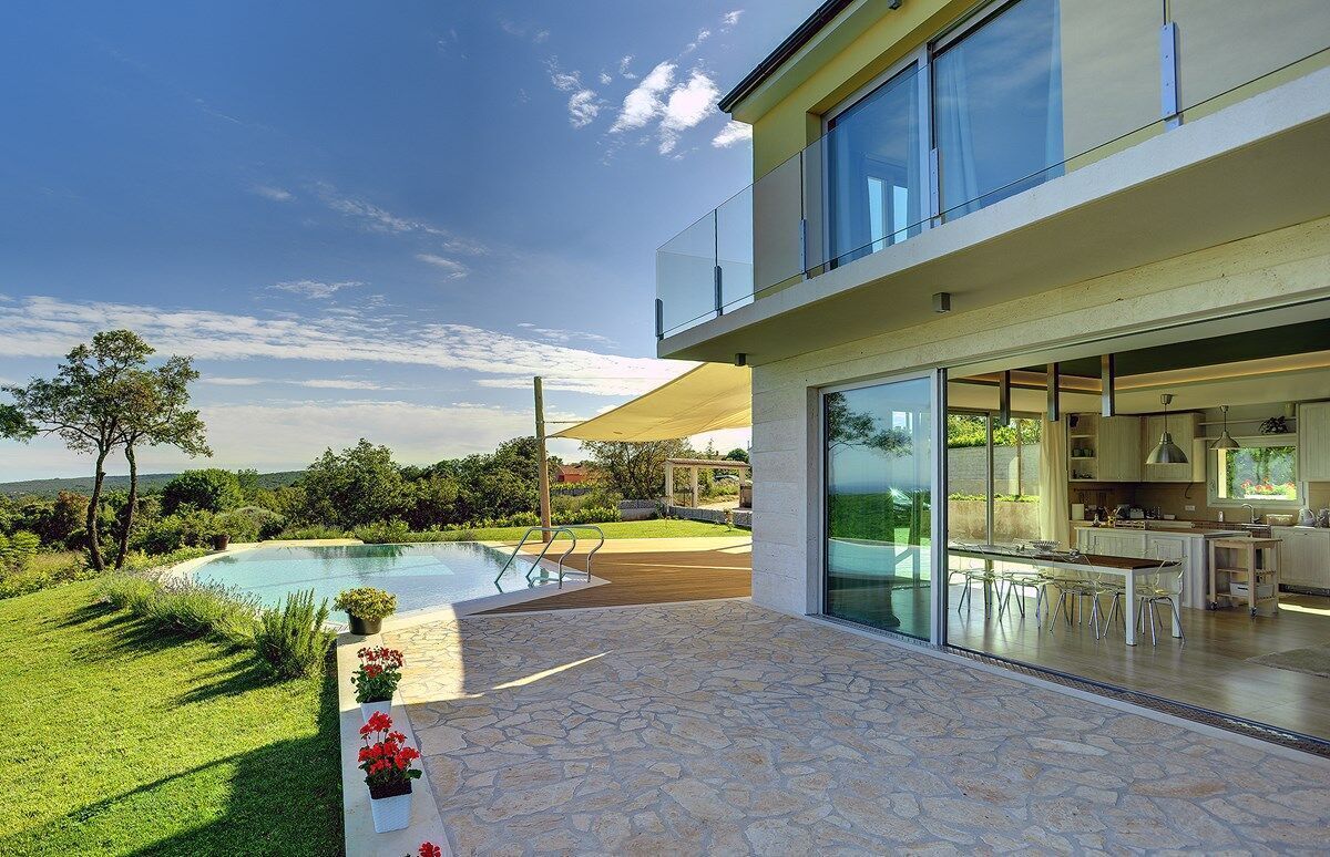 A modern house with a large glass balcony, a swimming pool, and a well-maintained garden.