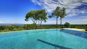 Una piscina infinita azul cristalina, con vistas al océano y árboles al fondo.
