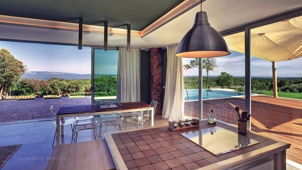 Una cocina moderna con una isla grande, un comedor con sillas y vistas a una piscina y jardines.