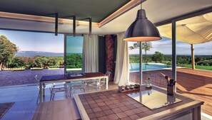 Eine moderne Küche mit einer großen Kochinsel, einem Essbereich mit Stühlen und Blick auf einen Pool und die Landschaft.