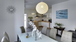 Et moderne køkken med hvide skabe, en hængende lampe og et maleri af en bølge på væggen.