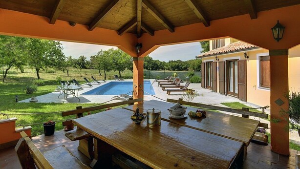 A covered outdoor seating area with a pool and lounge chairs, wooden tables, and a view of a garden and building. - Villa Fatima (V3497-K1) - Krnica (Pula) (Krnica (Pula))