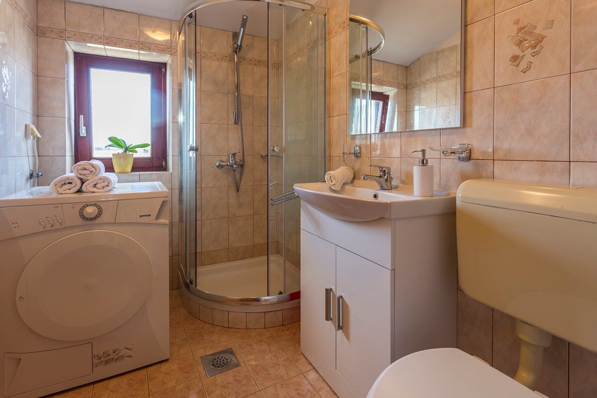 Un bagno compatto con lavatrice, box doccia in vetro e lavandino con specchio.